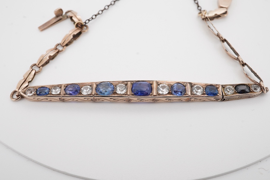 An early 20th century yellow metal and graduated two colour sapphire set line bracelet, with safety chain, gross weight 6.8 grams. Condition - fair